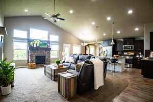 Living room featuring a stone fireplace, ceiling fan, high vaulted ceiling, recessed lighting, and dark wood-style floors