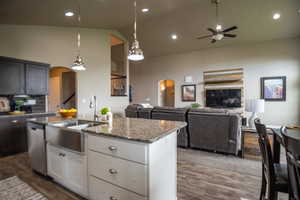 Kitchen featuring arched walkways, a ceiling fan, stainless steel dishwasher, open floor plan, and high vaulted ceiling