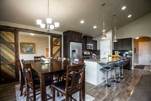 Dining room with a barn door, arched walkways, dark wood-style flooring, vaulted ceiling, and recessed lighting