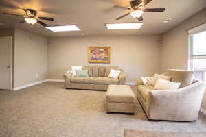 Carpeted living room with a skylight, ceiling fan, and baseboards