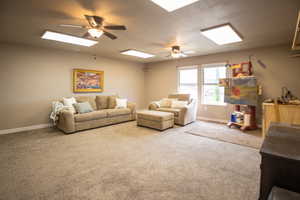 Carpeted living area with ceiling fan, a skylight, and baseboards