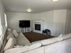 Living area featuring a fireplace with flush hearth, a decorative wall, carpet, a textured ceiling, and wainscoting
