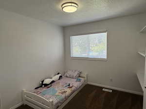 Bedroom with a textured ceiling, baseboards, and dark carpet