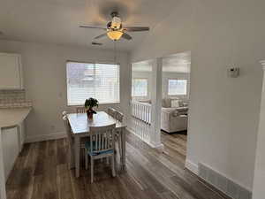Dining room with ceiling fan, dark wood-type flooring, baseboards, and vaulted ceiling