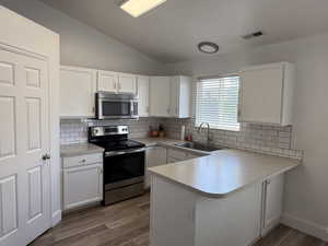 Kitchen featuring stainless steel appliances, a sink, vaulted ceiling, backsplash, and white cabinetry