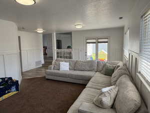 Carpeted living area featuring a decorative wall, a textured ceiling, and wainscoting