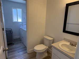 Bathroom with washing machine and clothes dryer, vanity, wood finished floors, toilet, and baseboards
