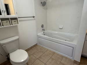 Full bathroom featuring a combined bath / shower with jetted tub, toilet, tile patterned floors, and baseboards