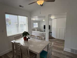 Dining area with wood finished floors, a ceiling fan, vaulted ceiling, wainscoting, and a decorative wall