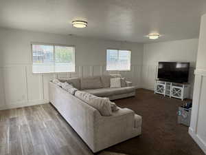 Living room featuring a decorative wall, a textured ceiling, healthy amount of natural light, a wainscoted wall, and wood finished floors