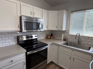 Kitchen with stainless steel appliances, a sink, light countertops, white cabinetry, and decorative backsplash