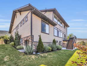 View of side of home featuring generous landscaping, fenced yard, board and batten siding, stone siding, and stairs