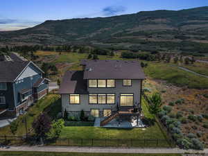 Back of house with stone siding, a patio area, a mountain view, borders open space, and a fenced backyard