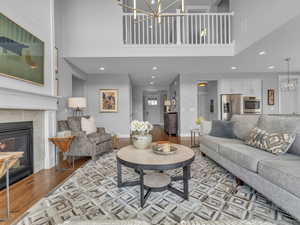 Living area featuring recessed lighting, wood finished floors, a chandelier, a fireplace, and a high ceiling