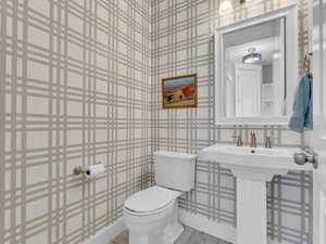Half bathroom featuring wallpapered walls and toilet
