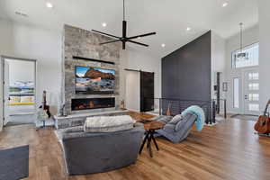 Living area featuring high vaulted ceiling, a stone fireplace, a ceiling fan, wood finished floors, and recessed lighting