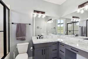 Bathroom with toilet, a shower with door, and double vanity