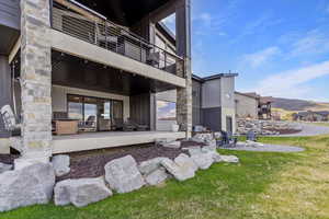 Back of property with a balcony, a patio area, and a lawn