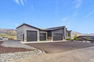 View of side of home with a mountain view, driveway, roof mounted solar panels, a garage, and stone siding