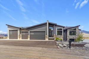 Contemporary house featuring stone siding, asphalt driveway, roof mounted solar panels, an attached garage, and a mountain view