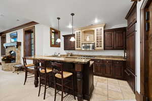 Kitchen featuring recessed lighting, dark brown cabinetry, stainless steel microwave, a kitchen bar, and dark stone counters