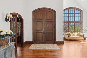 Entryway featuring dark wood-style flooring, a high ceiling, baseboards, and arched walkways