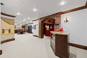 Interior space with baseboards, arched walkways, bar area, light carpet, and recessed lighting