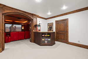 Cinema room featuring carpet flooring, baseboards, ornamental molding, and arched walkways