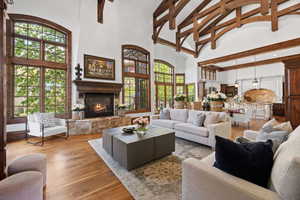 Living room with a wealth of natural light, wood finished floors, a stone fireplace, and high vaulted ceiling