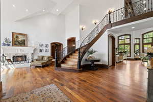 Stairs with arched walkways, a lit fireplace, wood-type flooring, and a high ceiling