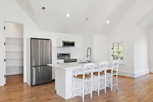 apartment Kitchen featuring lofted ceiling, light wood-style flooring, a sink, a kitchen breakfast bar, and appliances with stainless steel finishes