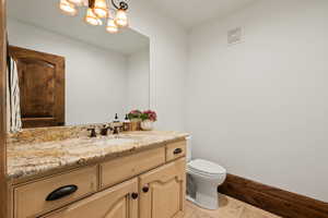 Half bathroom with toilet, baseboards, visible vents, vanity, and a chandelier