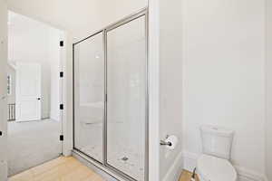 apartment Full bath featuring toilet, baseboards, a shower stall, and wood finished floors