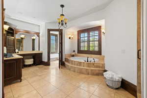 Bathroom featuring vanity, tile patterned floors, an inviting chandelier, baseboards, and a bath