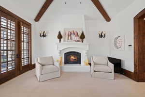 Sitting room featuring a lit fireplace, carpet, and vaulted ceiling with beams