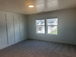 Spare room featuring dark colored carpet, a textured ceiling, and baseboards