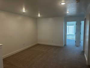 Spare room with dark carpet, baseboards, a textured ceiling, and a smoke detector