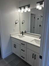Full bath with tile patterned flooring, a shower stall, double vanity, and baseboards