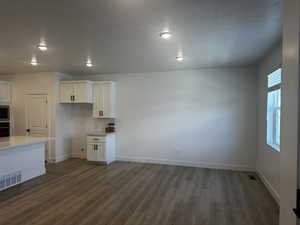 Unfurnished dining area with dark wood finished floors, a textured ceiling, baseboards, and recessed lighting