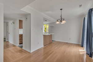 Unfurnished dining area featuring a chandelier, light wood-style floors, baseboards, and ornamental molding