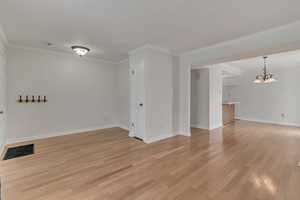 Empty room with a chandelier, light wood-style floors, baseboards, and ornamental molding