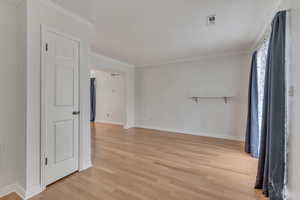Empty room with light wood-style flooring, baseboards, and crown molding