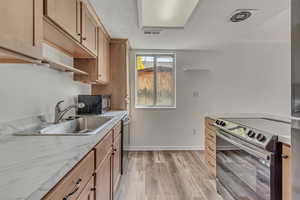 Kitchen featuring appliances with stainless steel finishes, a sink, baseboards, light brown cabinetry, and light wood-style flooring