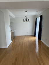 Unfurnished dining area with a chandelier, light wood-type flooring, ornamental molding, and baseboards
