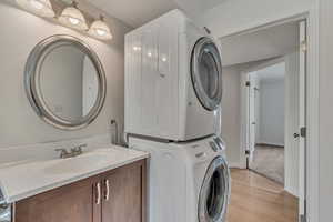 Clothes washing area with estacked washer and dryer, a sink, light wood-type flooring, and baseboards