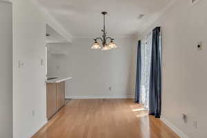 Unfurnished dining area featuring light wood finished floors, a chandelier, baseboards, healthy amount of natural light, and ornamental molding