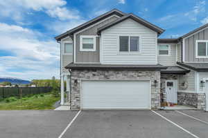 Multi unit property featuring board and batten siding, stone siding, driveway, an attached garage, and a mountain view