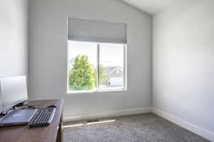 Carpeted empty room with healthy amount of natural light, baseboards, vaulted ceiling, and a desk