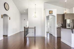 Kitchen featuring arched walkways, stainless steel fridge, a chandelier, high vaulted ceiling, and dark wood-style floors