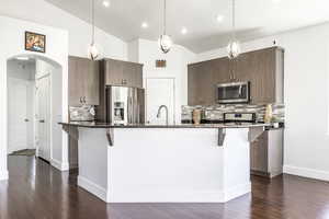 Kitchen with appliances with stainless steel finishes, arched walkways, a kitchen breakfast bar, tasteful backsplash, and dark wood-style flooring